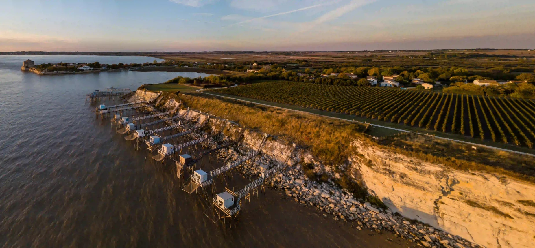 Camping à Talmont-sur-Gironde en Charente-Maritime, vue aérienne au coucher du soleil des carrelets en bord de falaise et des vignobles.